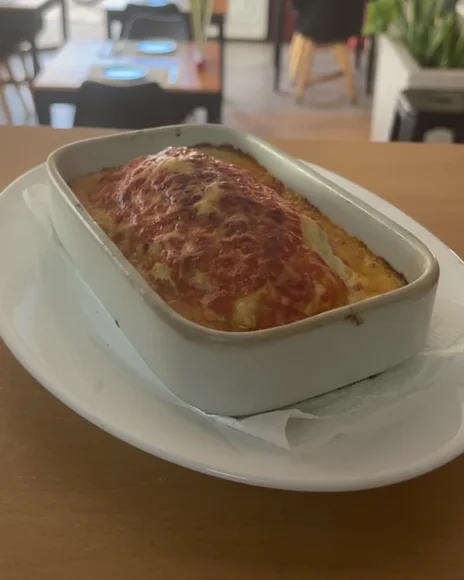 Fuente de pasta gratinada al horno con queso dorado, sobre un plato blanco en el local